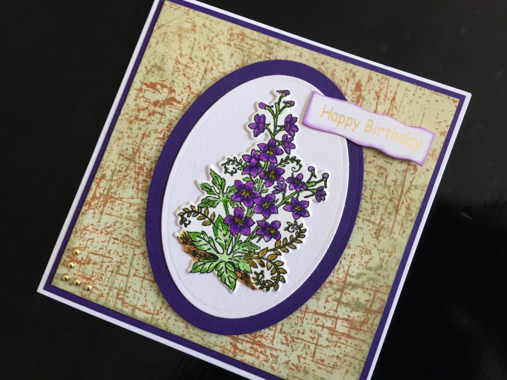 Hand made birthday card with stamped and die cut larkspur, on a stamped and inked background.