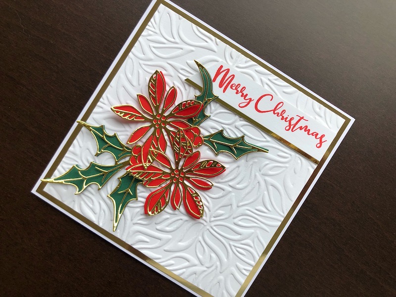 Hand made Christmas card with die cut layered poinsettia and holly on an embossed background