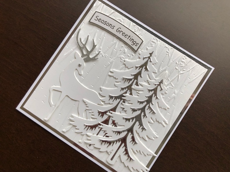 Hand made Christmas card with die cut reindeer and winter pine trees