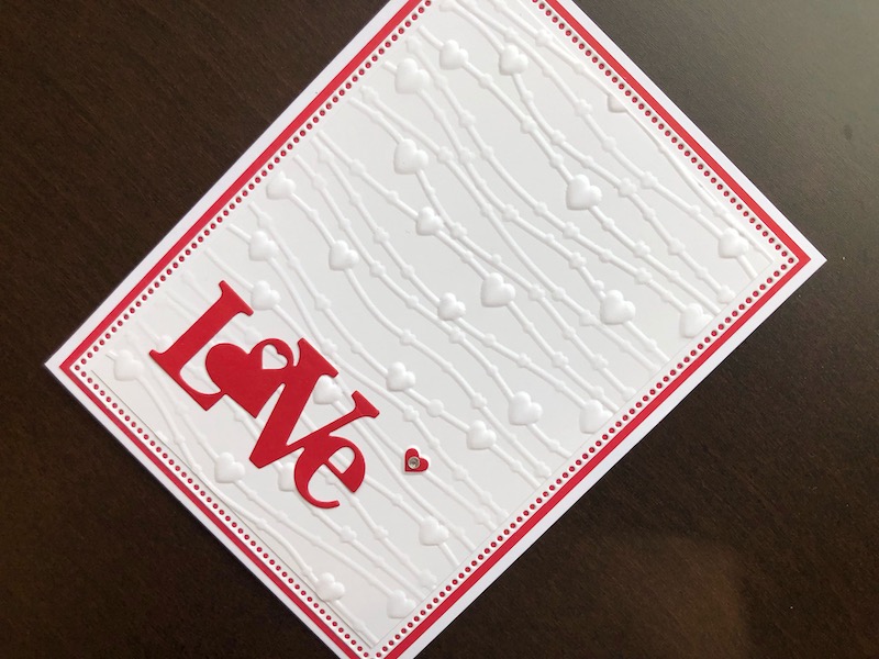 Hand made Valentine card with hearts on a string embossed background and die cut love sentiment