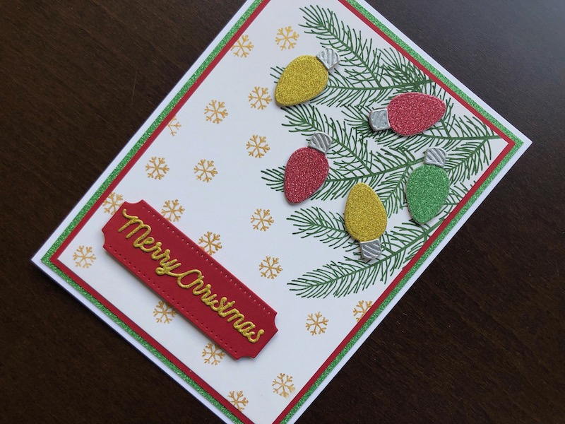 Hand made Christmas card with stamped pine branches and snowflakes and die cut Christmas lights and sentiment