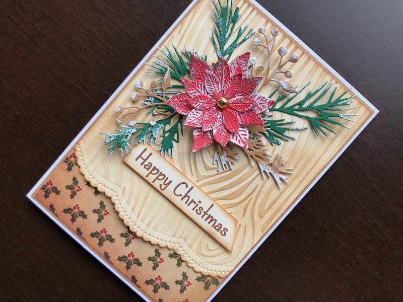 Hand made Christmas card with die cut poinsettia and foliage on an embossed woodgrain background