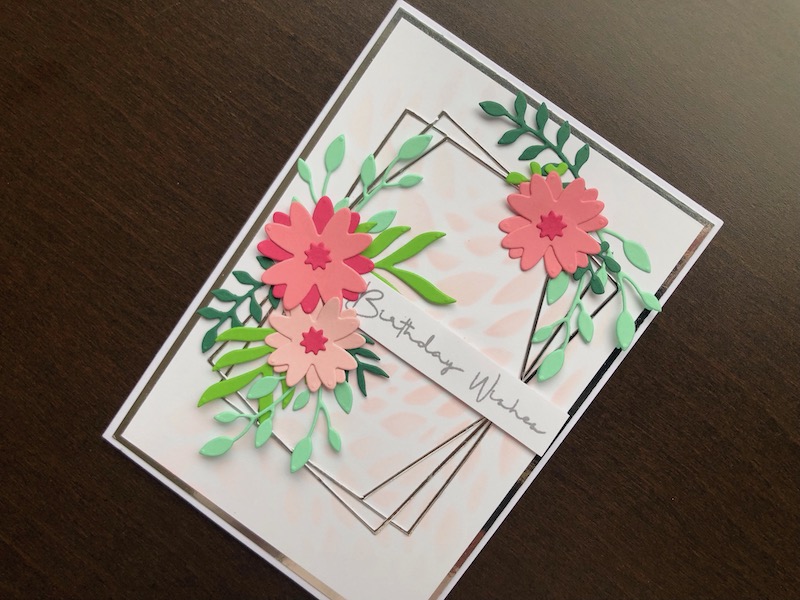 A hand made birthday card with stencilled background and die cut frames, flowers and foliage.