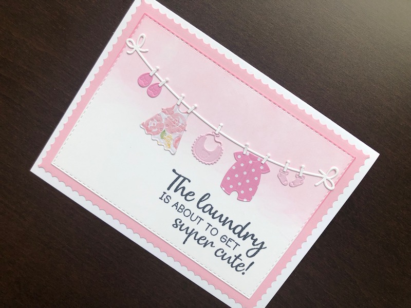 Hand made new baby card in pink with die cut baby clothes on a washing line.