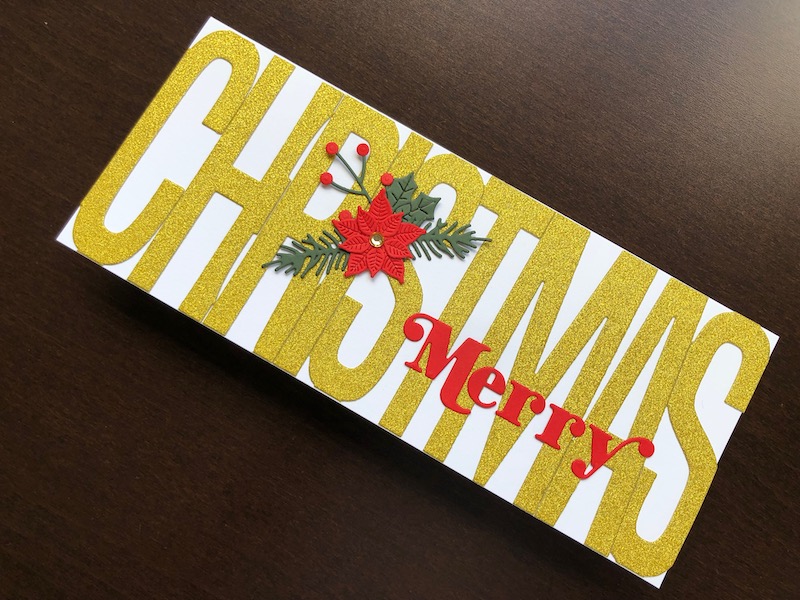 Hand made Christmas card with bold die cut gold glitter lettering and winter foliage and poinsettia.