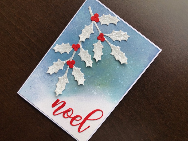 Hand made Christmas card with inked background, holly branches with chunky glitter and red noel sentiment