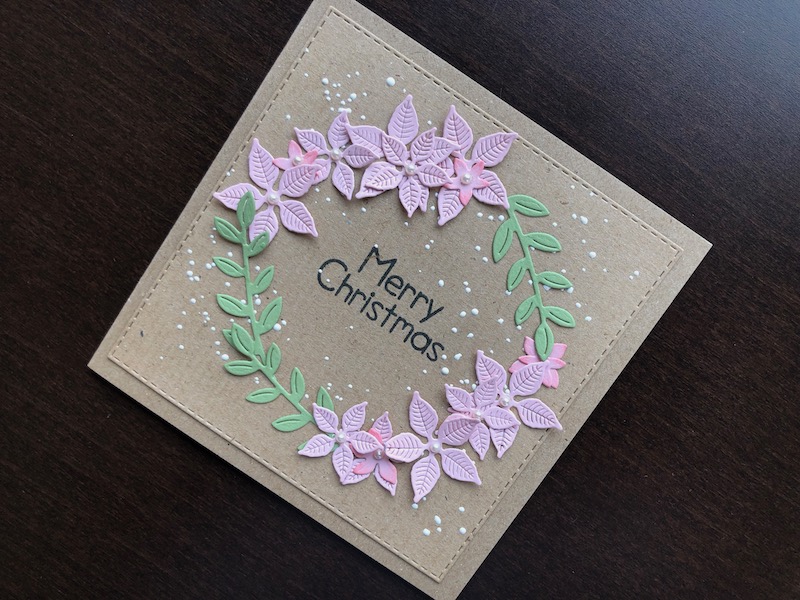 Hand made Christmas card with a wreath of die cut pink poinsettias and leafy stems on a kraft background.
