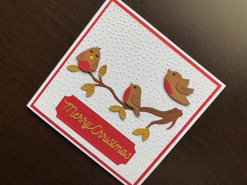 Hand made Christmas card with embossed snowfall background and die cut robins on a branch.