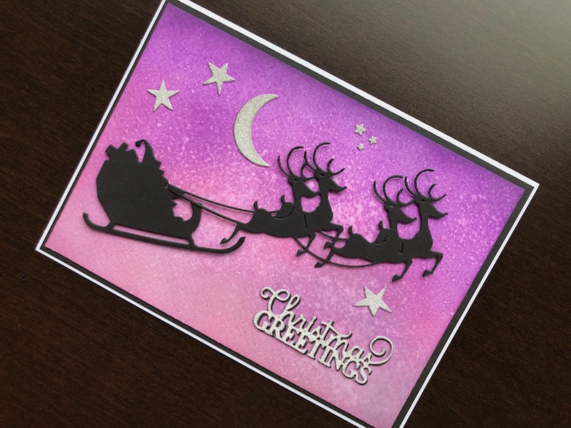 Hand made Christmas card with inked night sky background and die cut silhouette Santa and reindeer sleigh.