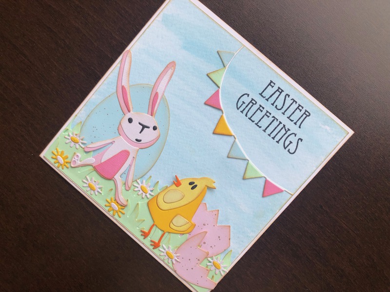 Hand made Easter card with die cut eggs, bunny, chick, grass and flowers on an ink wash background.